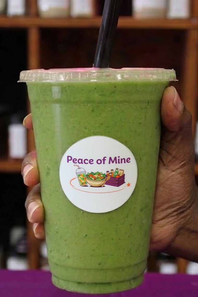 A green sea moss smoothie held up in front of the Peace of Mine shelves