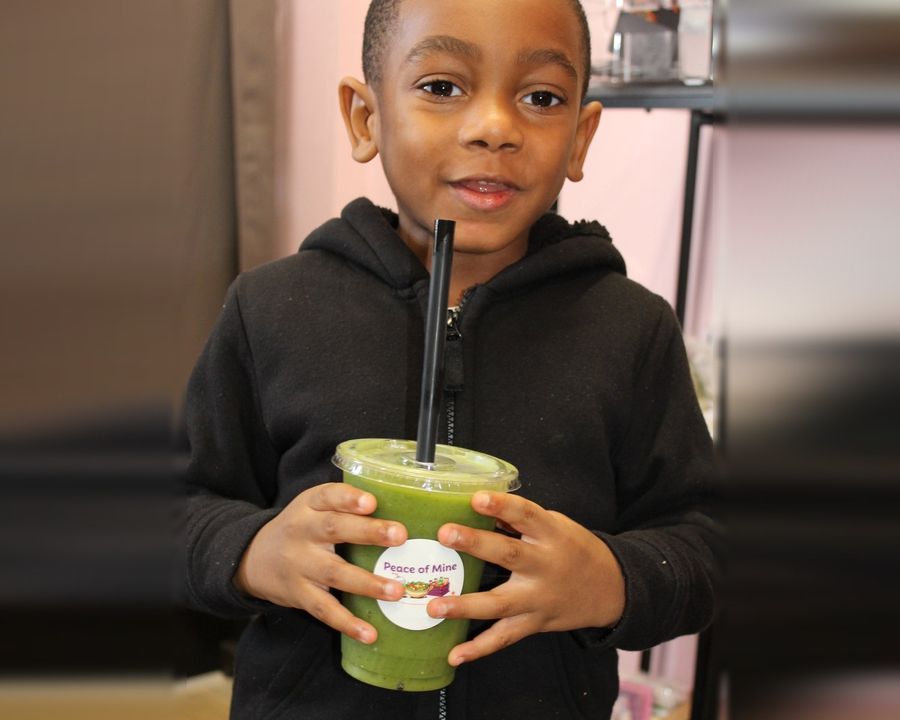 A smiling kid holding a green Peace of Mine smoothie in the shop