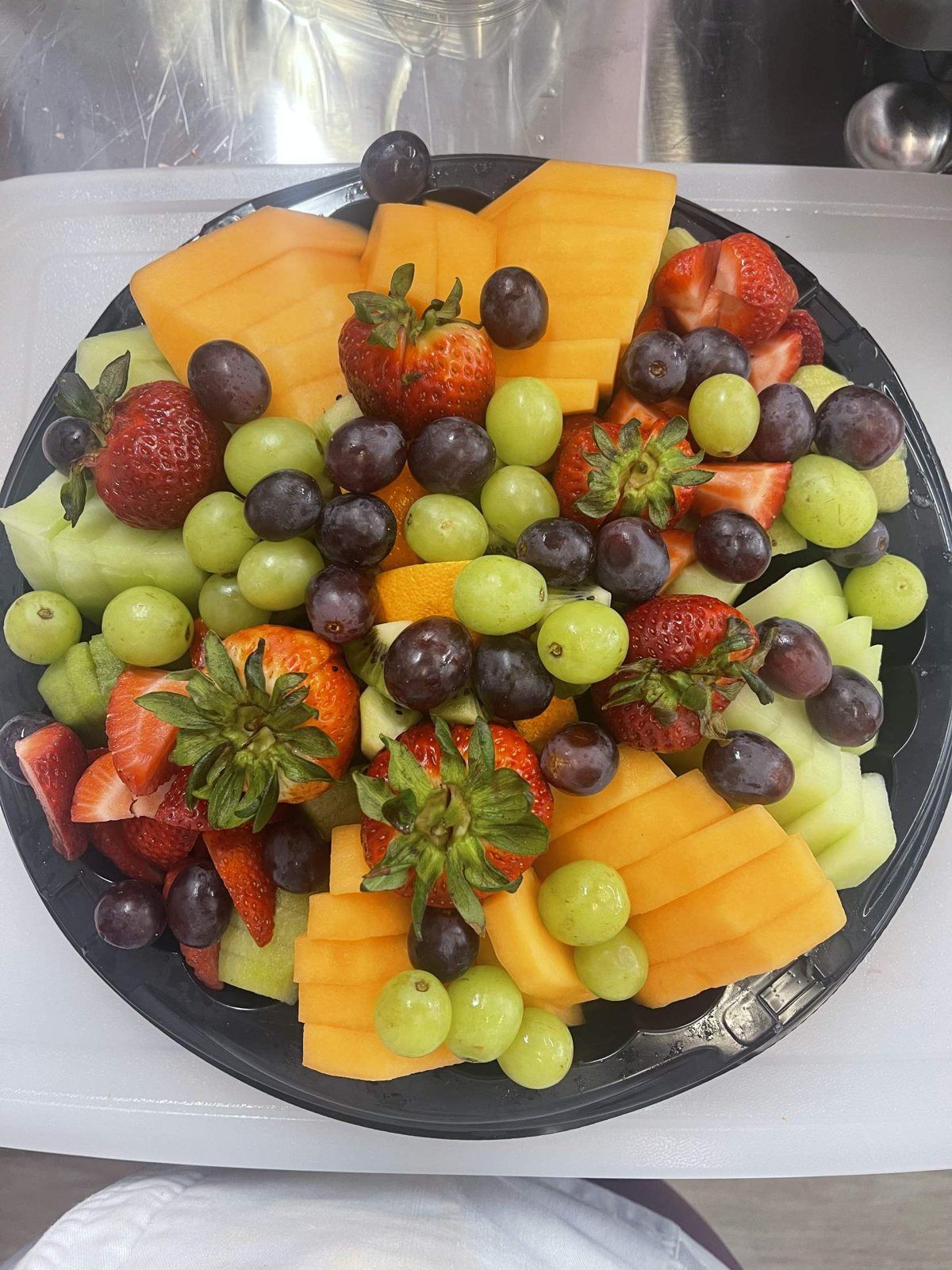 A round tray of cut cantaloupe, honeydew, strawberries and grapes