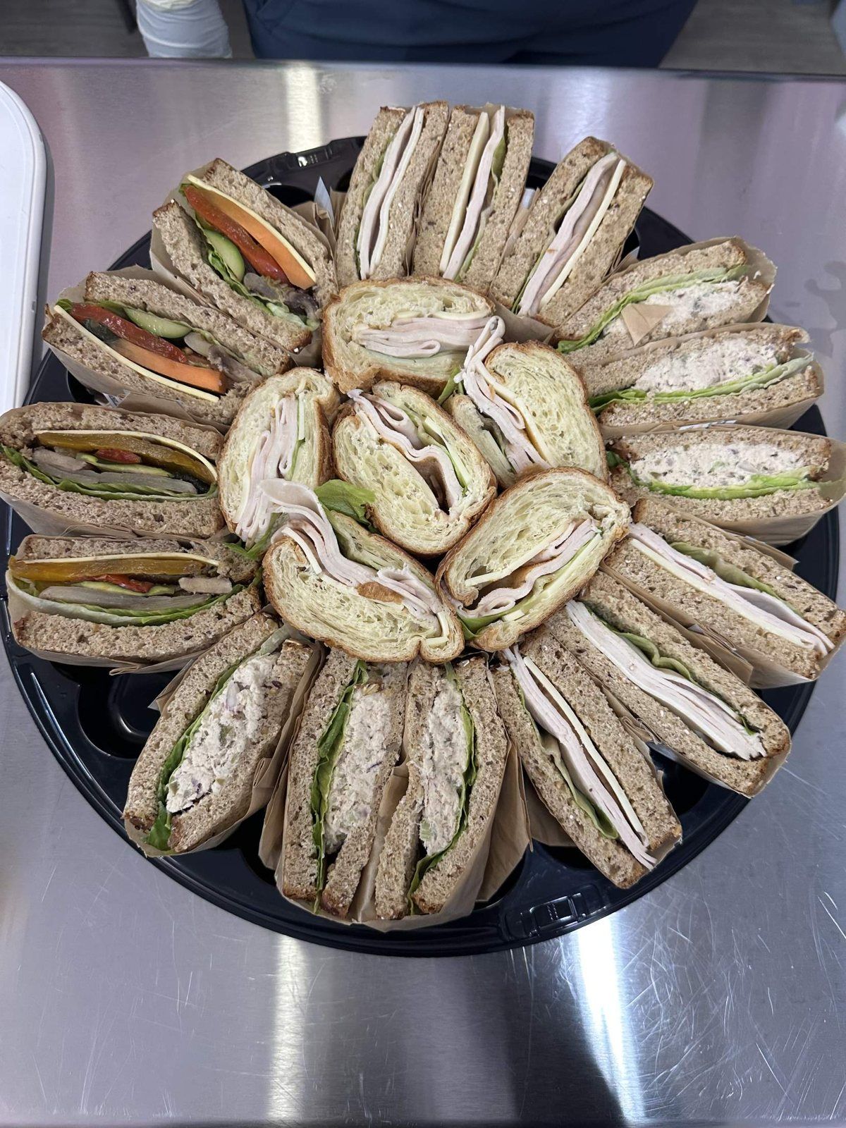 A round platter of wrapped sandwiches and turkey croissants