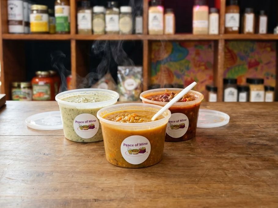 Three Peace of Mine soups on the shop counter, lids off and steaming: lentil, broccoli and veggie chili